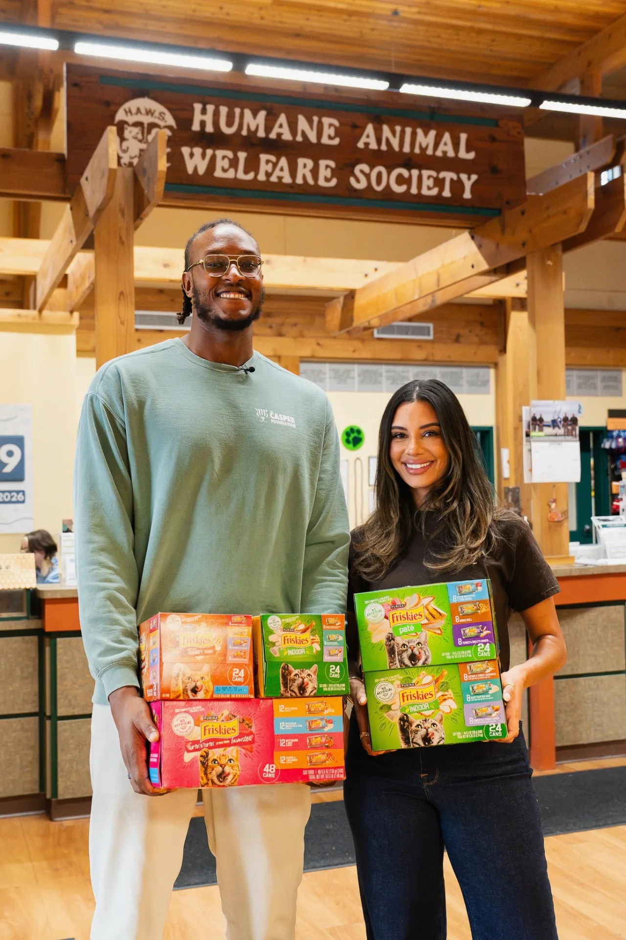 Myles and Aysia holding cases of Friskies wet food at the Humane Animal Welfare Society